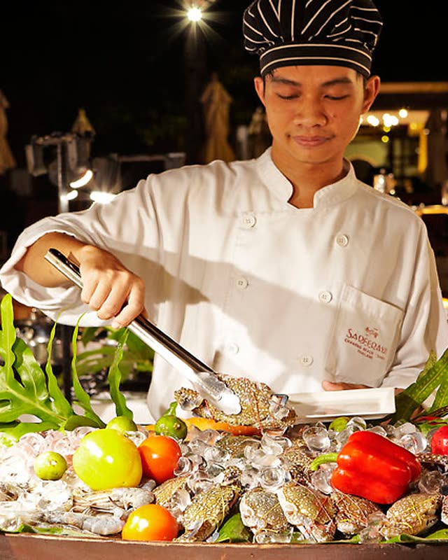 Chef in whites serving from a display of seafood, fruit and vegetables at night