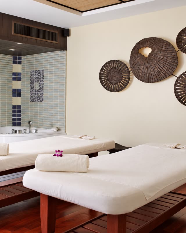 Spa room with two white massage beds and woven plates on the wall