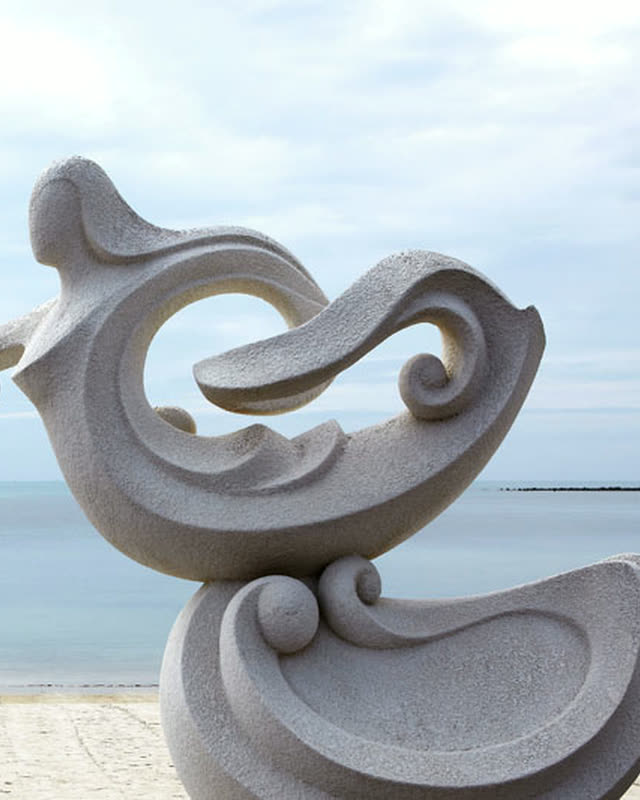 Carved stone sculpture on the sand with the calm sea behind