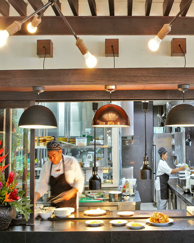 Open kitchen with copper pendant lamps, chefs at work and red heliconia flowers