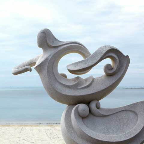 Carved stone sculpture on the sand with the sea behind