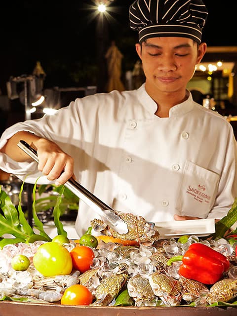 Chef serving seafood from a display on ice with fruit and vegetables