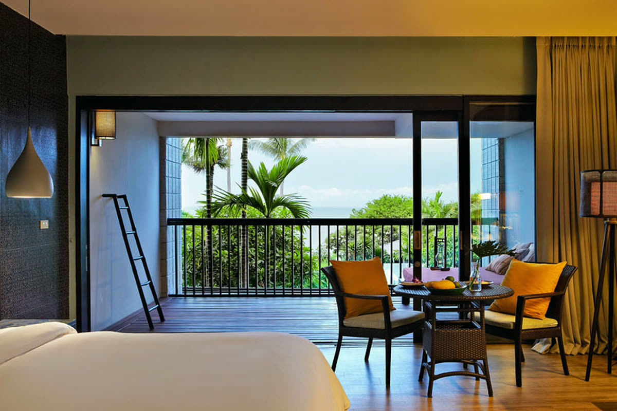 Room opening to a balcony with a table and two chairs, palms and sea beyond