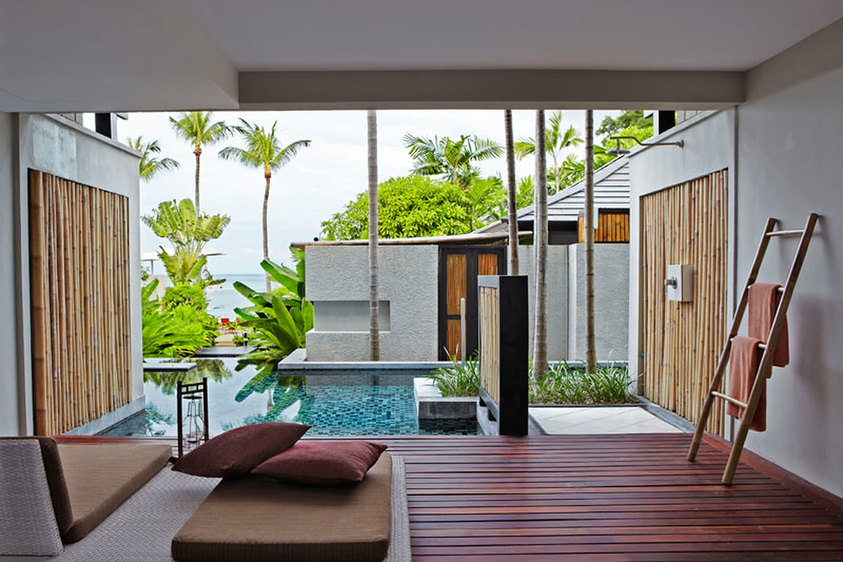 Timber terrace with a daybed and bamboo screens beside a tiled pool, palms and sea beyond